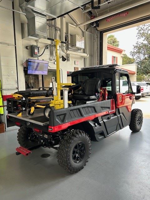 A red and black off-road rescue vehicle sits in a fire station bay, carrying a yellow lift system.