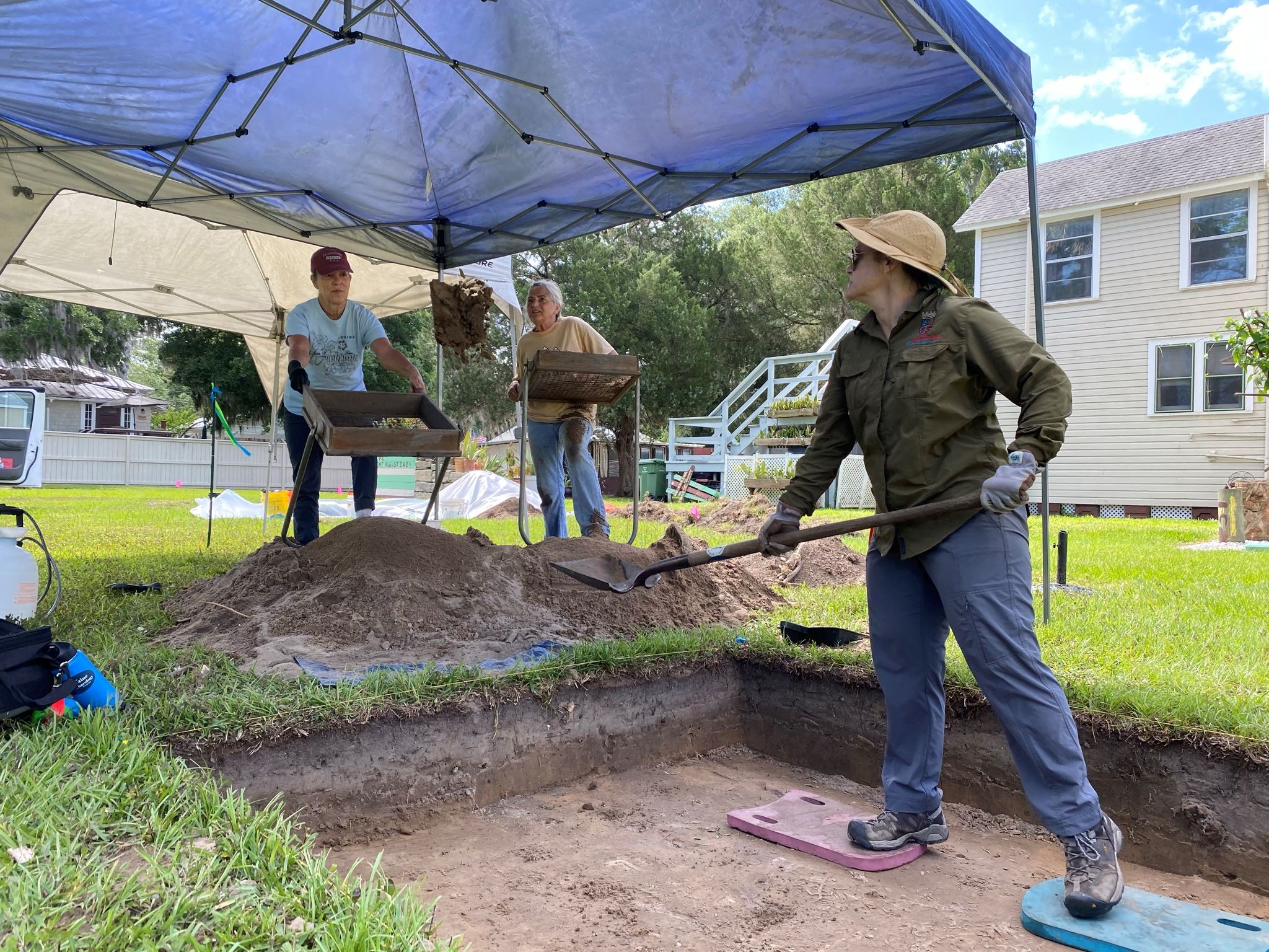 One person shoveling in an excavation unit with two people screening nearby